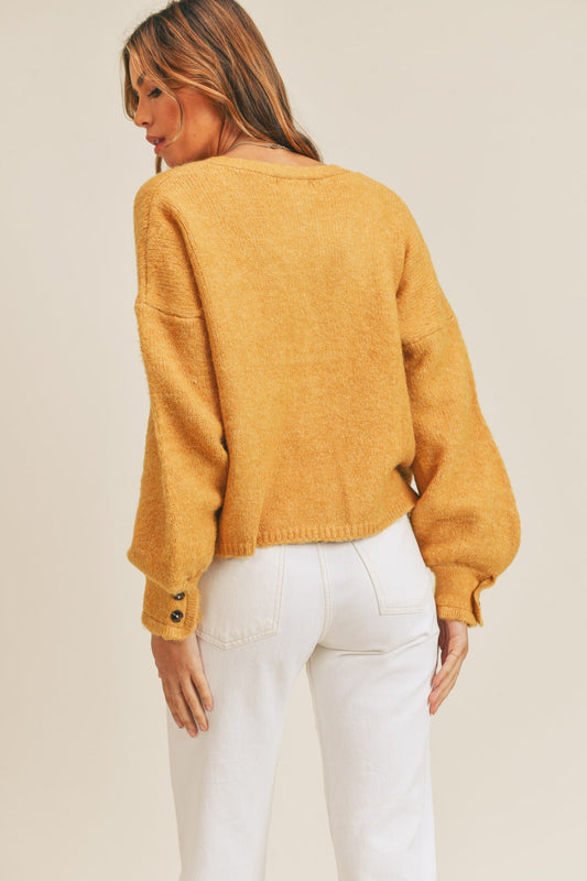 Woman wearing a mustard long sleeve button down sweater cardigan with slightly stretchy fabric composition of acrylic, polyester, and spandex.