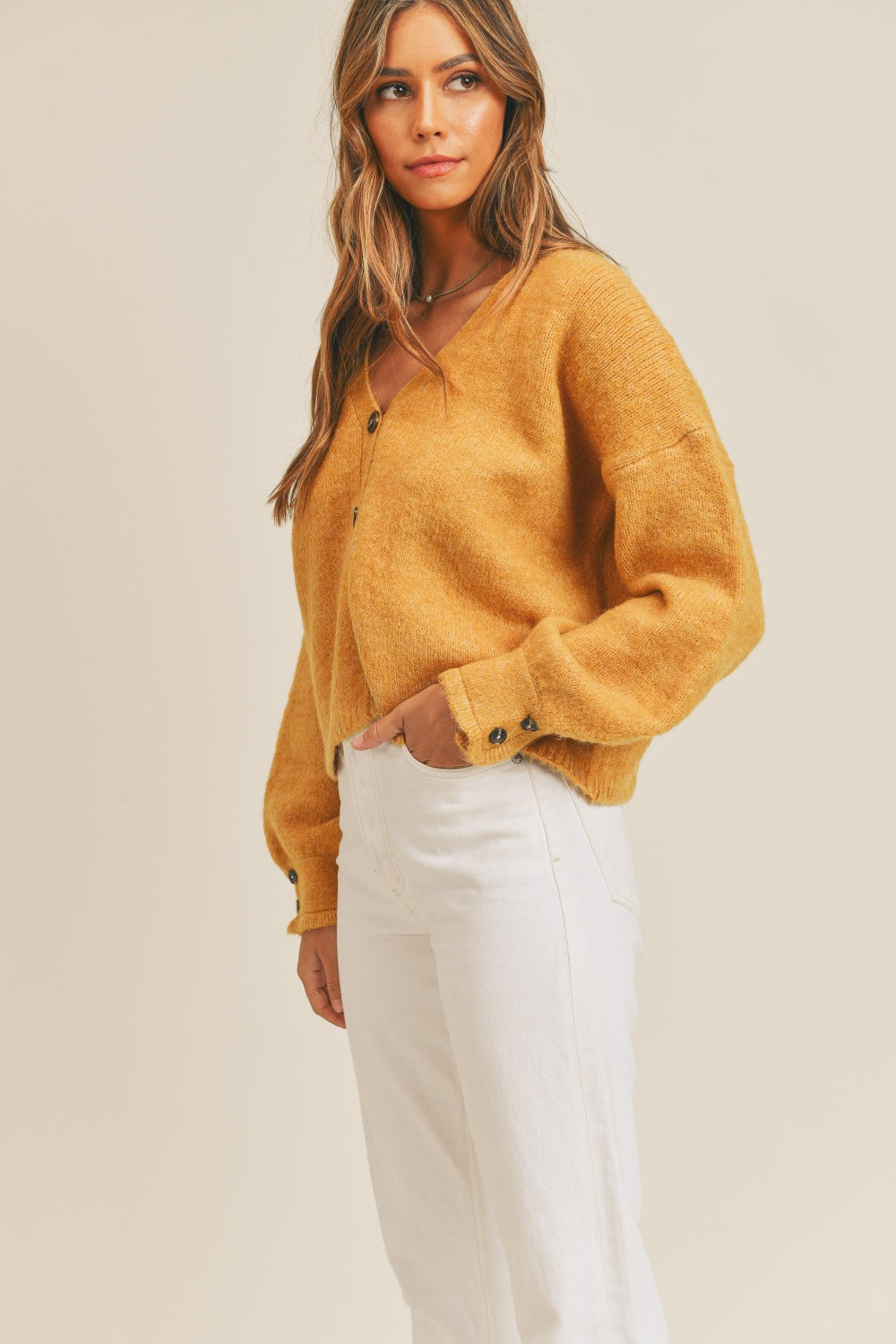 Woman wearing a mustard long sleeve button down sweater cardigan with white pants.