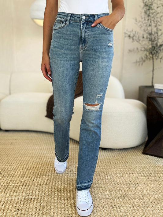 Woman wearing mid-rise distressed hem jeans with moderate stretch, featuring a basic style and a ripped knee design.