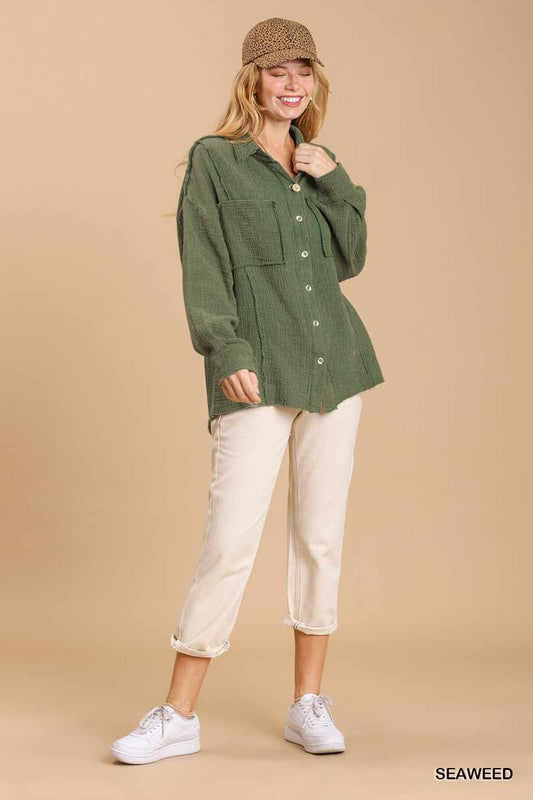 Woman wearing a seaweed green mineral wash button down top with high low hem, paired with cream pants and white sneakers.