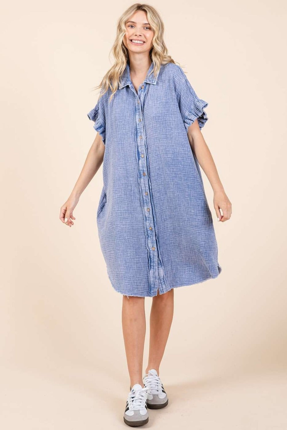 Woman wearing a blue mineral wash cotton gauze mini shirt dress with buttoned front, ruffled sleeves, and raw hem.