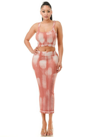 Woman in coral pink tie-dye ribbed two-piece set with crop top and midi skirt, posing with hand on hip against white background, wearing nude strap...