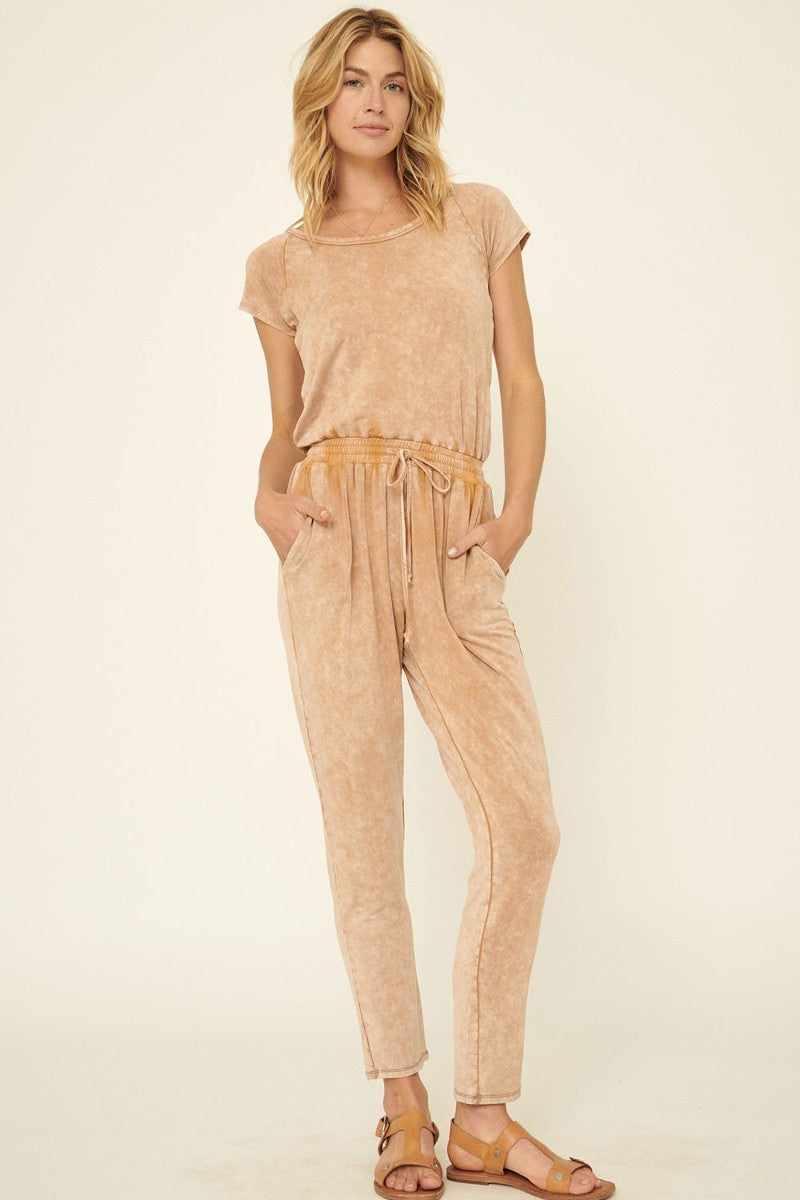 Mineral washed knit jumpsuit with scoop neckline, drawstring waist, and side pockets, featuring short sleeves and tapered cuffed legs.