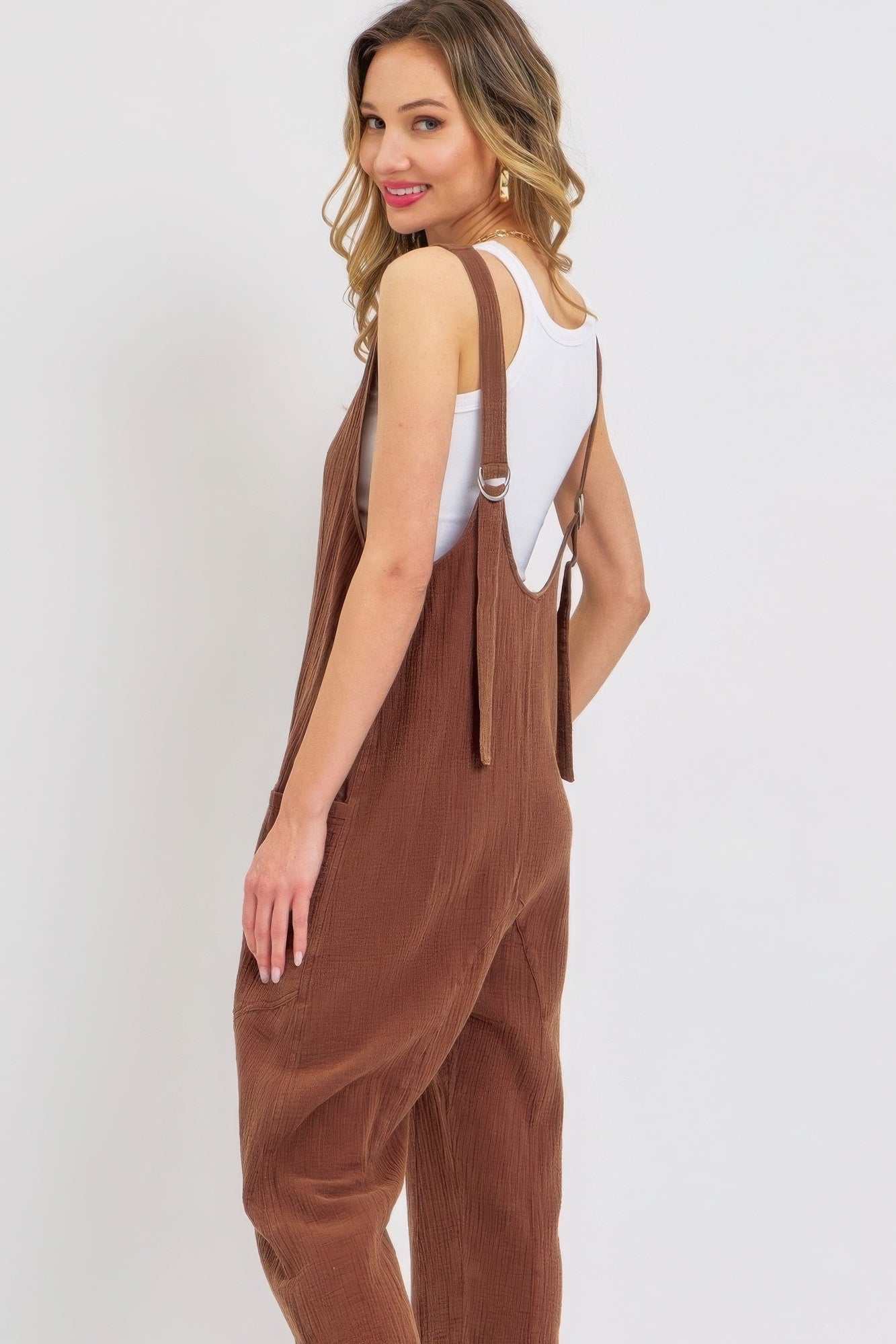 Woman wearing a brown mineral washed summer jumpsuit with adjustable straps and oversized pockets, perfect for relaxed summer style.