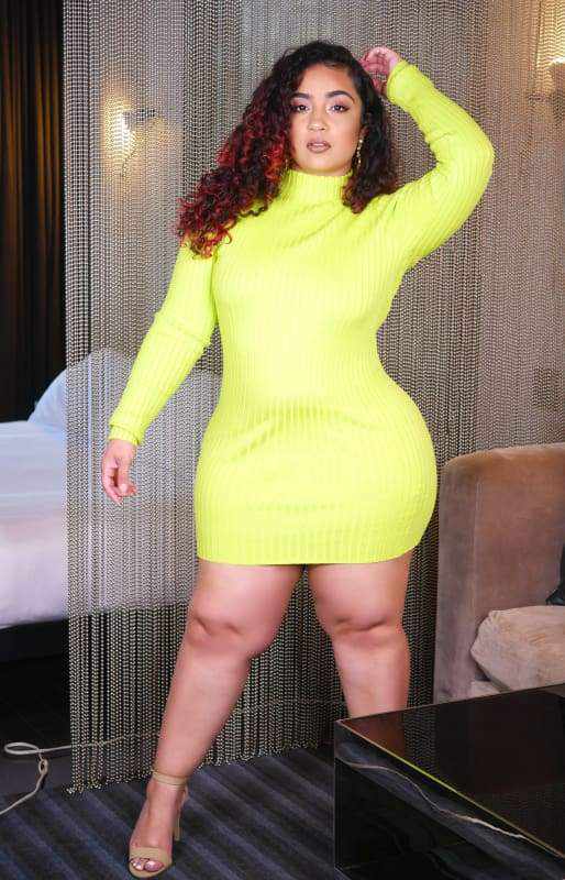 Woman in lime green mini dress, standing with hand on head, highlighting fashion style and comfort indoors.