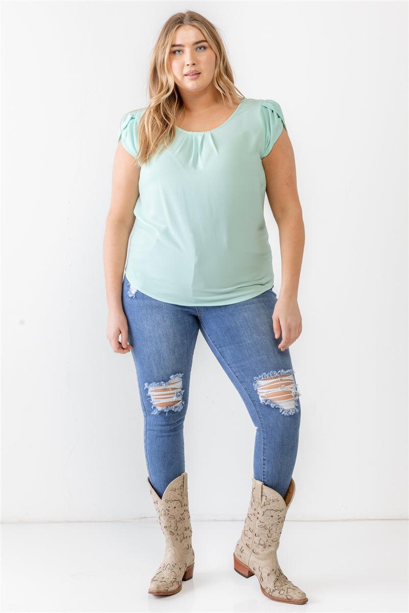 Plus size model wearing a mint textured short sleeve blouse with cap sleeves and crew neckline, paired with ripped jeans and boots.