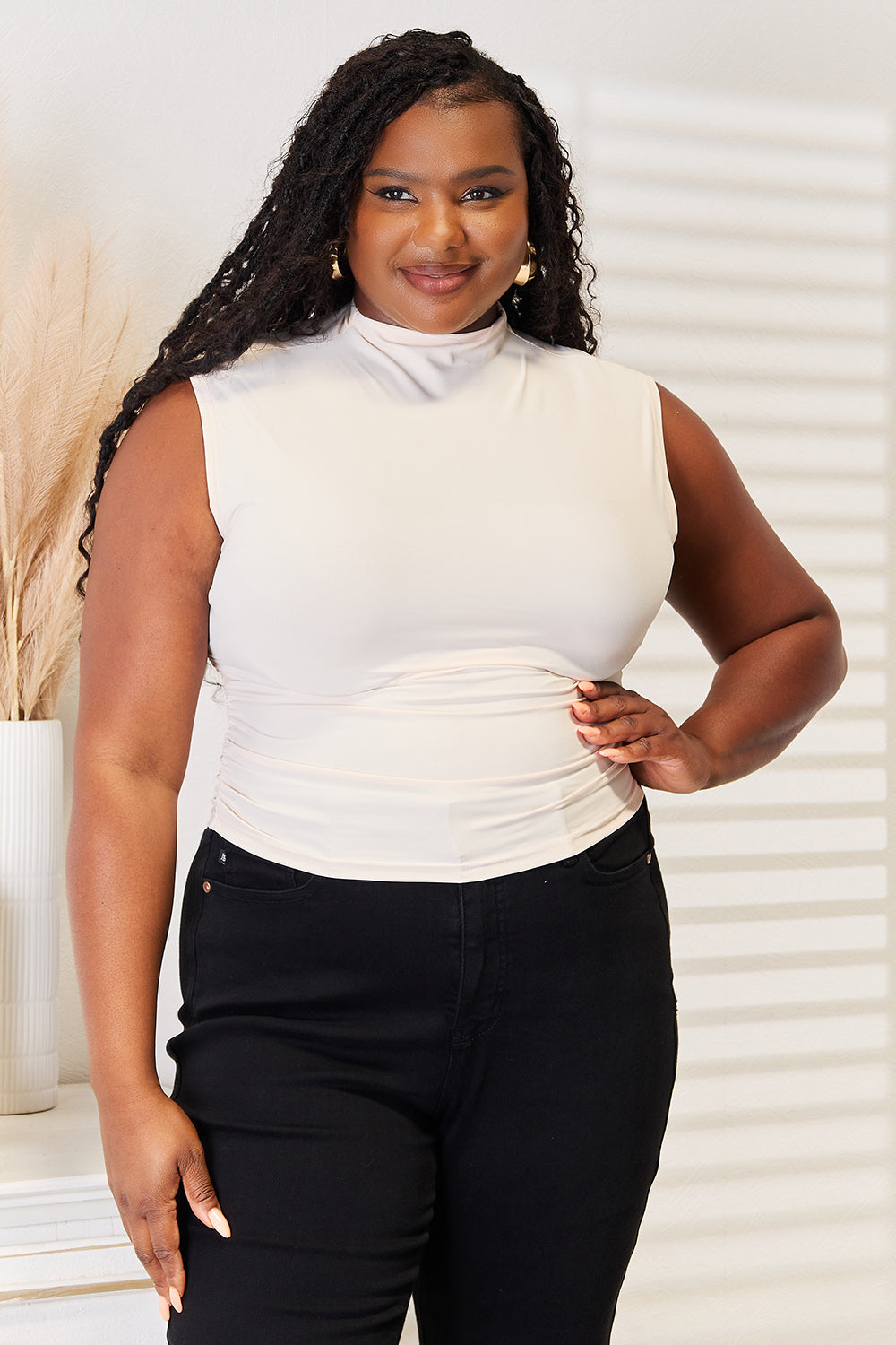 Woman wearing mock neck ruched cropped tank in white, paired with black jeans, showcasing a flattering and comfortable fit.