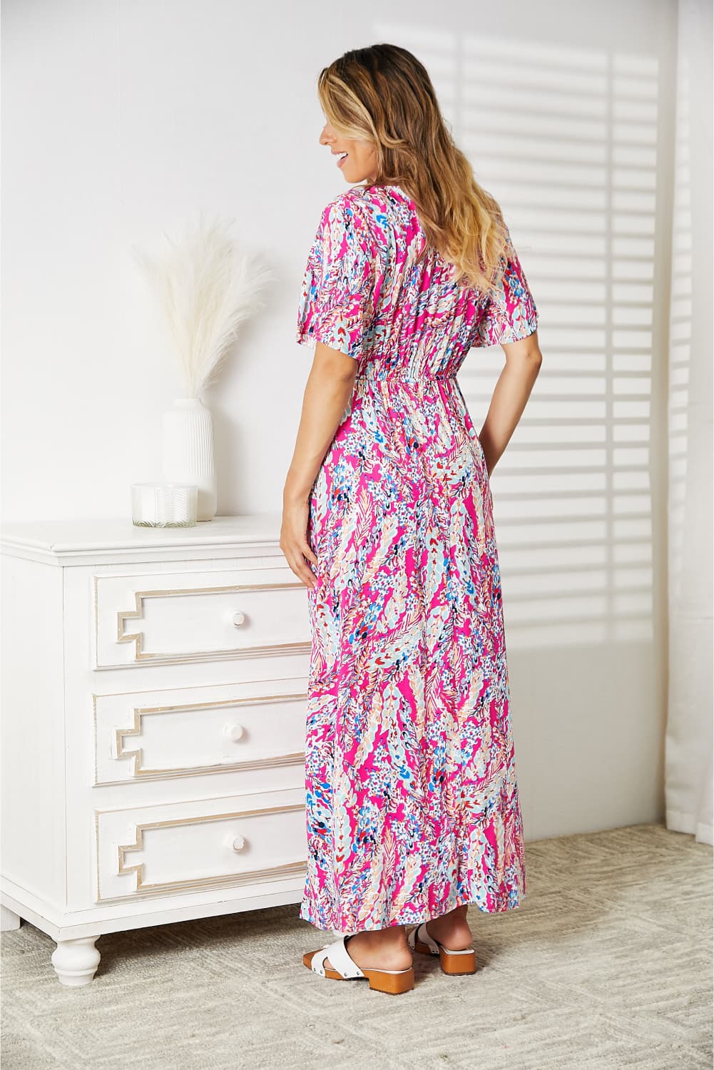 Woman wearing Double Take Multicolored V-Neck Maxi Dress stands beside white dresser in sunlit room.