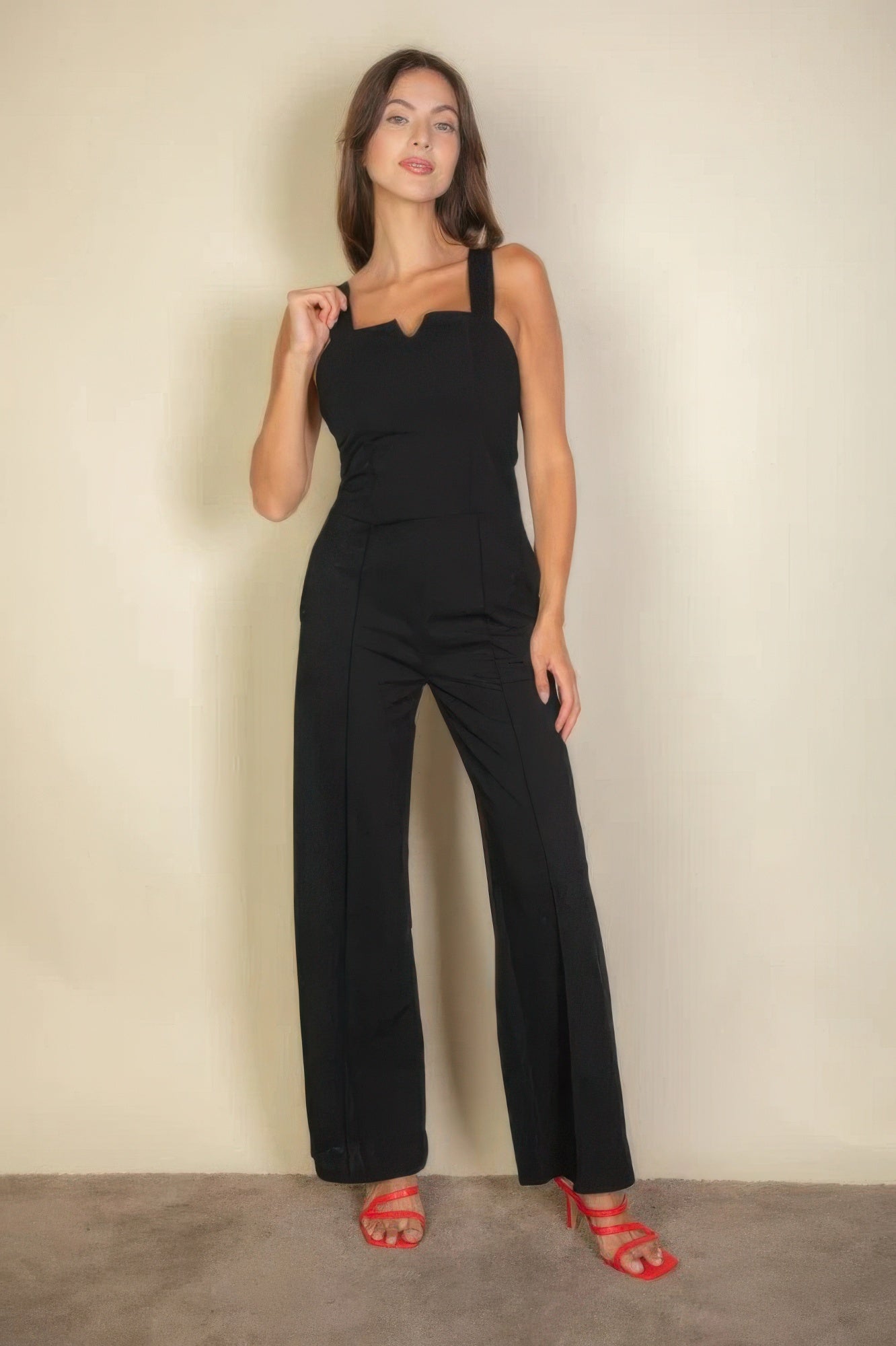 Woman wearing a black notched neck cami jumpsuit with red sandals, showcasing a chic and modern style in a tailored fit.