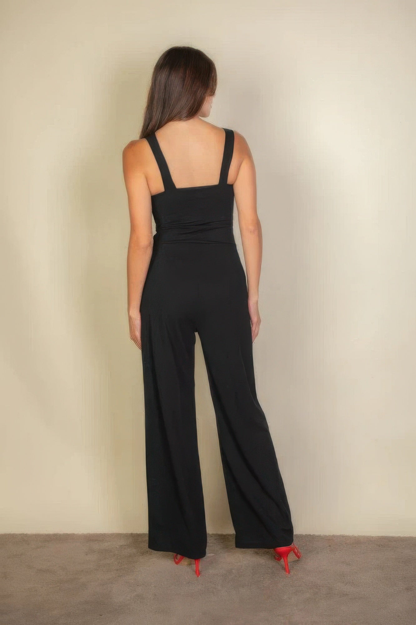 Woman wearing black notched neck cami jumpsuit with red heels, showcasing a chic, tailored fit from the back.