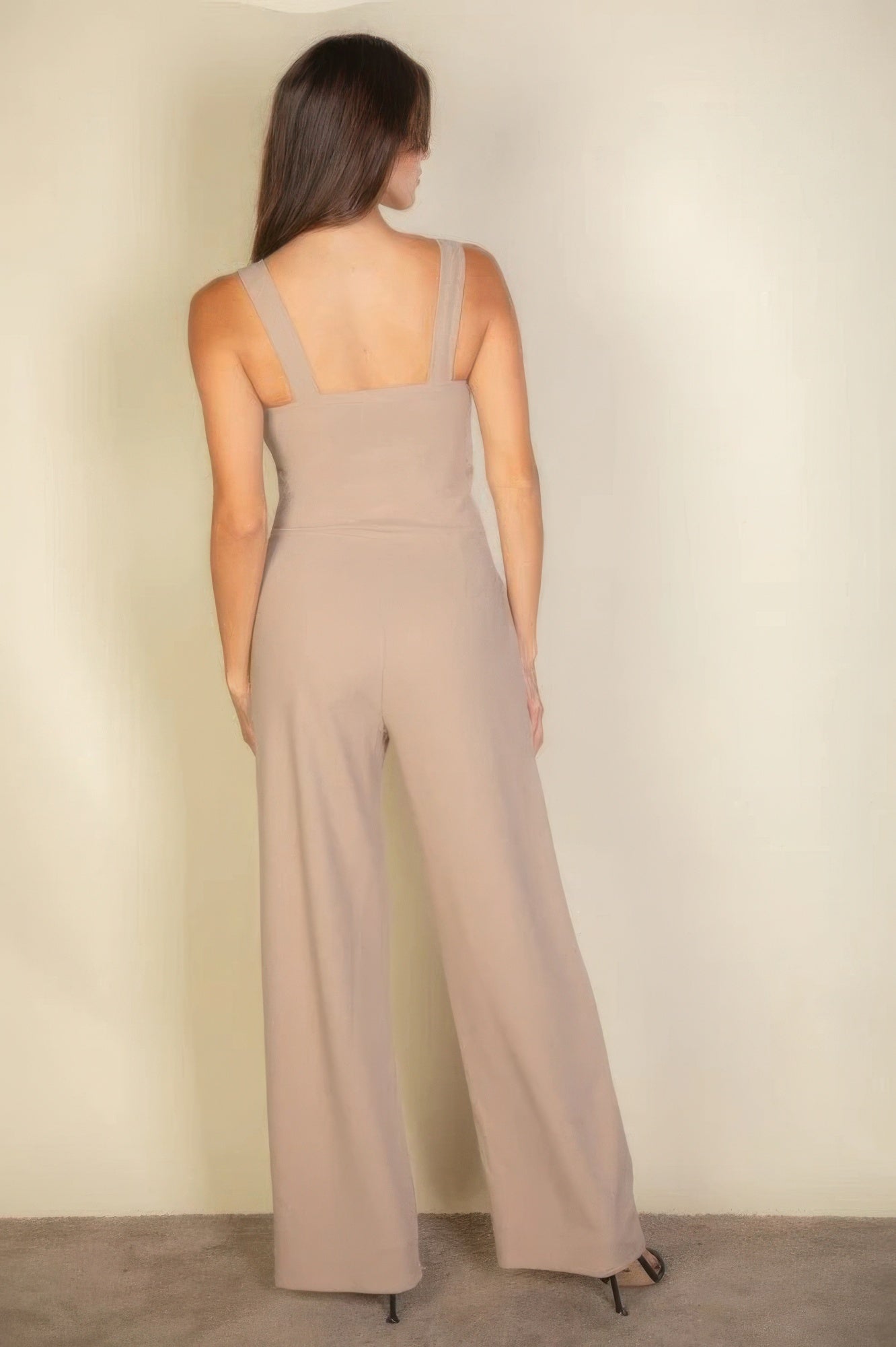 Back view of woman wearing taupe notched neck cami jumpsuit, showcasing sleek fit and modern style.