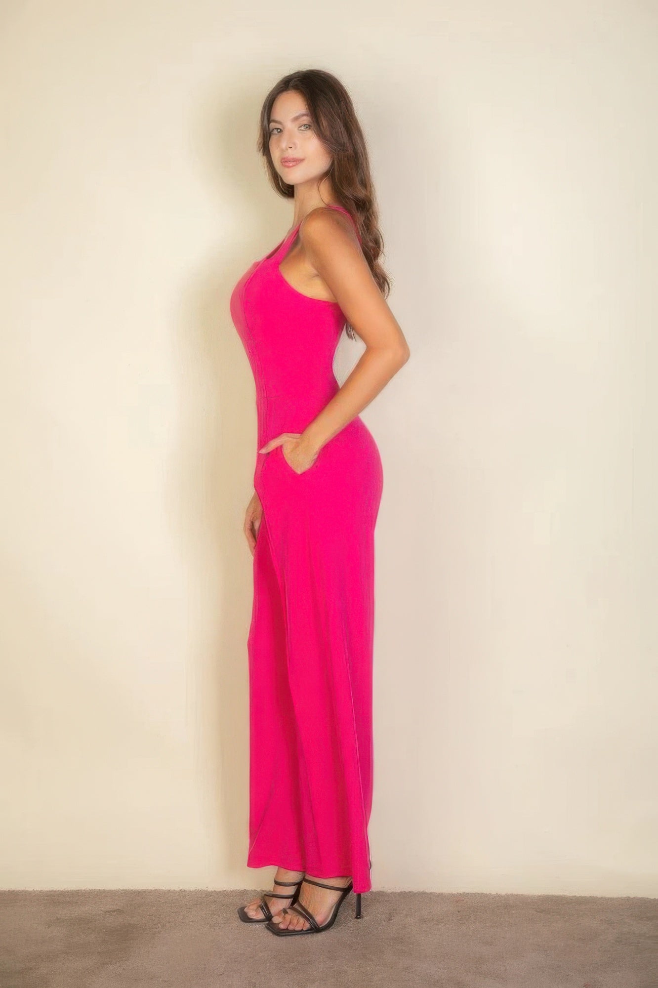 Woman wearing a bright pink sleeveless jumpsuit and black heels, standing confidently against a neutral background.