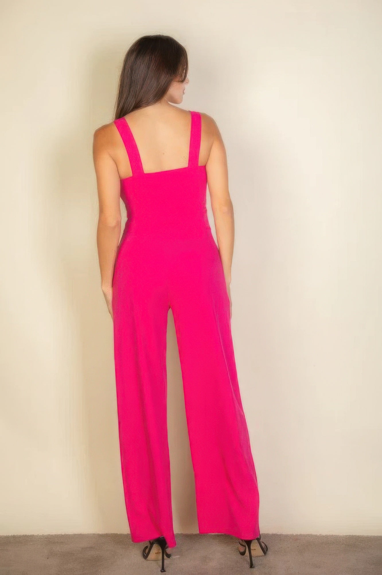 Woman wearing vibrant pink jumpsuit with square neckline and straps, showcasing chic and stylish fashion from the back.