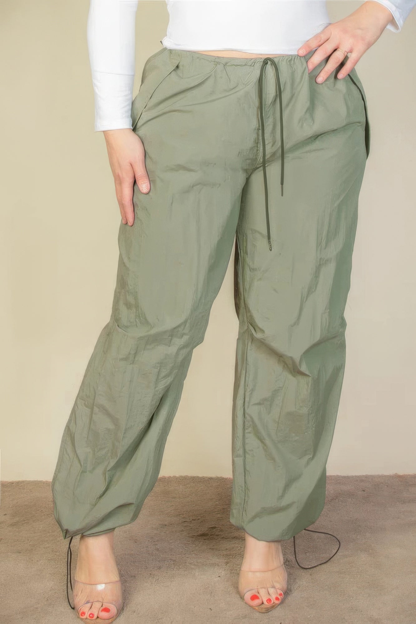 Woman wearing plus size drawstring waist parachute pants in olive green with toggle tighten and elastic band.