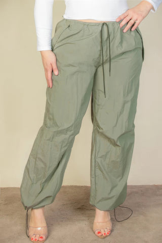 Woman wearing plus size drawstring waist parachute pants in olive green with toggle tighten and elastic band.