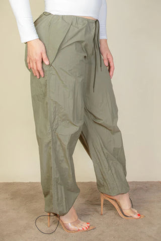 Plus size drawstring waist parachute pants in olive green, featuring elastic waistband and toggle tighten, styled with heels.