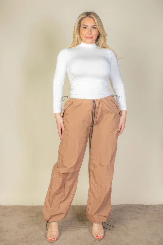 Plus size model wearing brown drawstring waist parachute pants and white top, showcasing comfort and style.