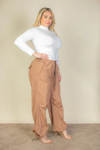 Plus size model wearing drawstring waist parachute pants in beige with a white top, showcasing a stylish and comfortable look.