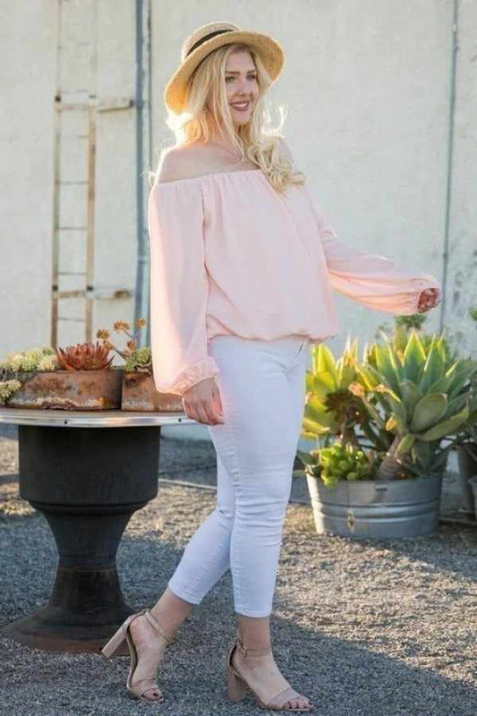 Woman wearing off shoulder long bubble sleeve solid top in rose, paired with white pants and a straw hat, outdoors.