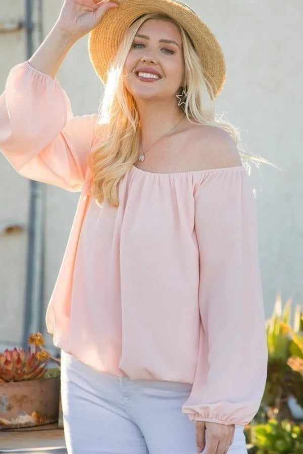 Woman in off shoulder long bubble sleeve top and hat, enjoying sunny day outdoors.