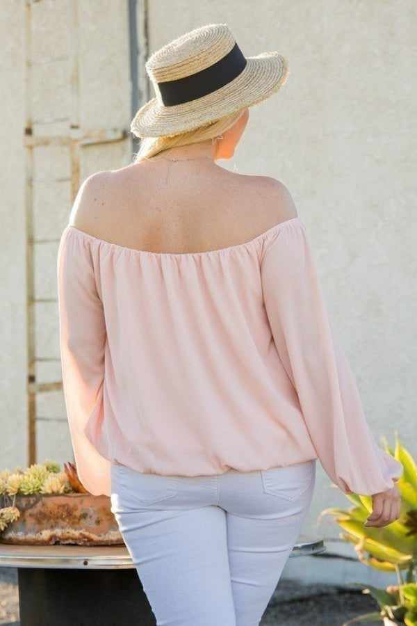 Woman wearing off shoulder long bubble sleeve solid top in rose, paired with white jeans and a straw hat.