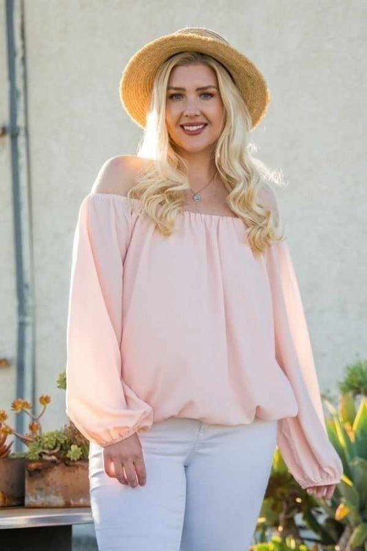 Woman wearing off shoulder long bubble sleeve solid top in rose color, styled with a straw hat, standing in a sunny outdoor setting.