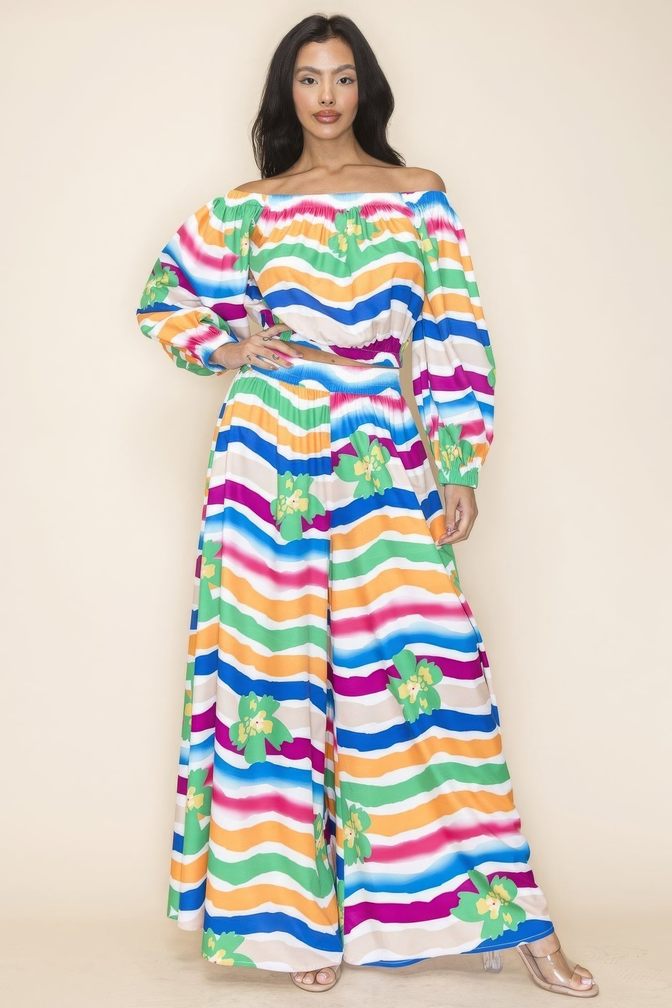 Woman wearing vibrant off-shoulder top and wide pants set with multi-color design, featuring elastic neckline and high-waisted pants.