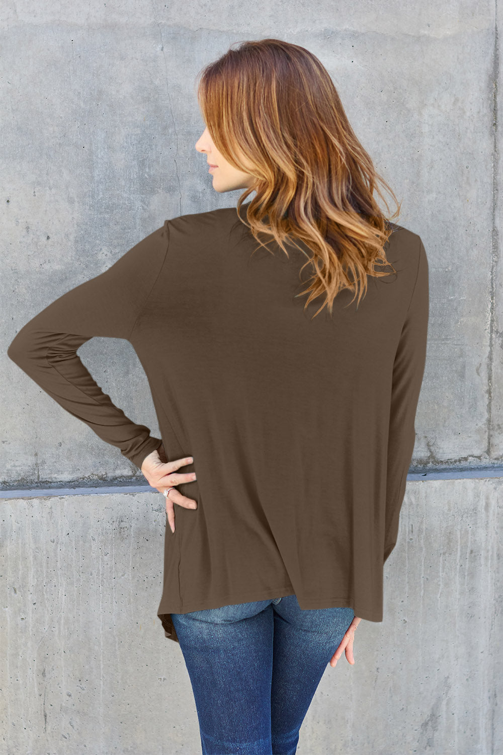 Woman wearing brown open front long sleeve cardigan made of rayon and spandex, back view against concrete wall.