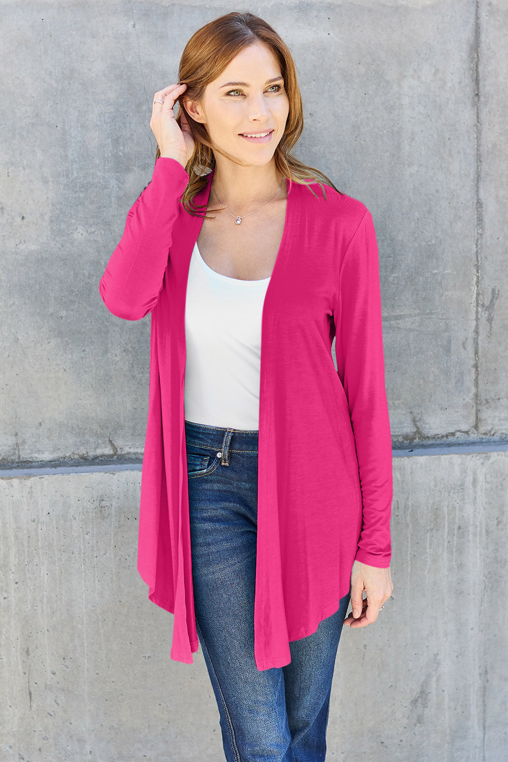 Woman wearing open front long sleeve cardigan in pink, paired with jeans and a white top, showcasing casual style.