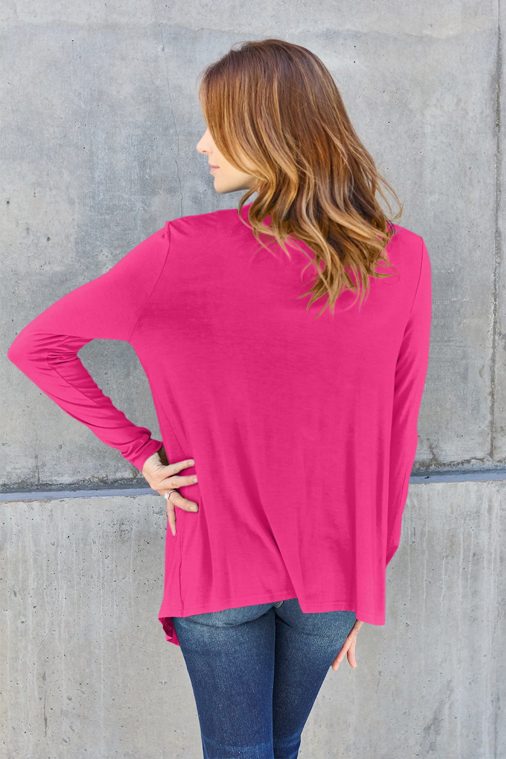 Woman wearing open front long sleeve pink cardigan, showing back view with slightly stretchy rayon-spandex blend, paired with jeans.