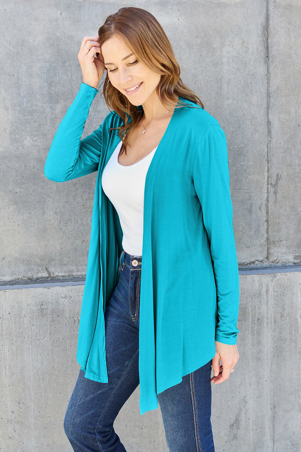 Woman wearing turquoise open front long sleeve cardigan over white top and jeans.