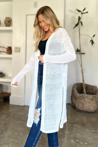 Woman wearing a white open front longline cardigan with openwork design and moderate stretch, made of 100% polyester.