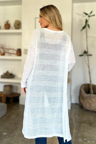 Woman wearing open front longline cardigan with openwork design, showcasing moderate stretch and polyester material in a stylish room.