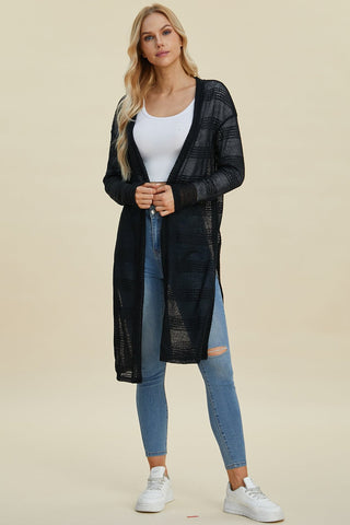 Woman wearing open front longline black cardigan with moderate stretch and openwork design, paired with jeans and sneakers.