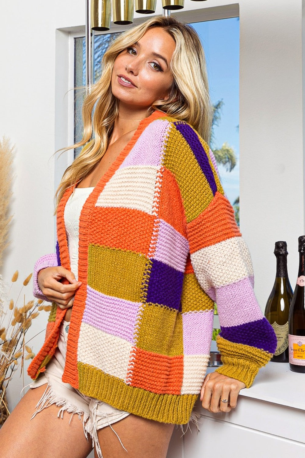 Woman wearing an orange checkered color block sweater cardigan with open front design and vibrant colors.