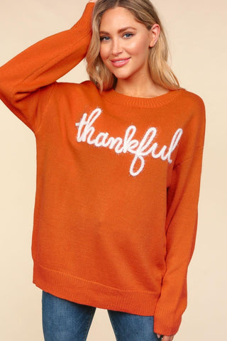 Woman wearing orange sweater with "thankful" text, paired with jeans, showcasing casual fall fashion.