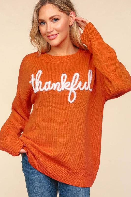 Woman wearing burnt orange "thankful" sweater with blue jeans.