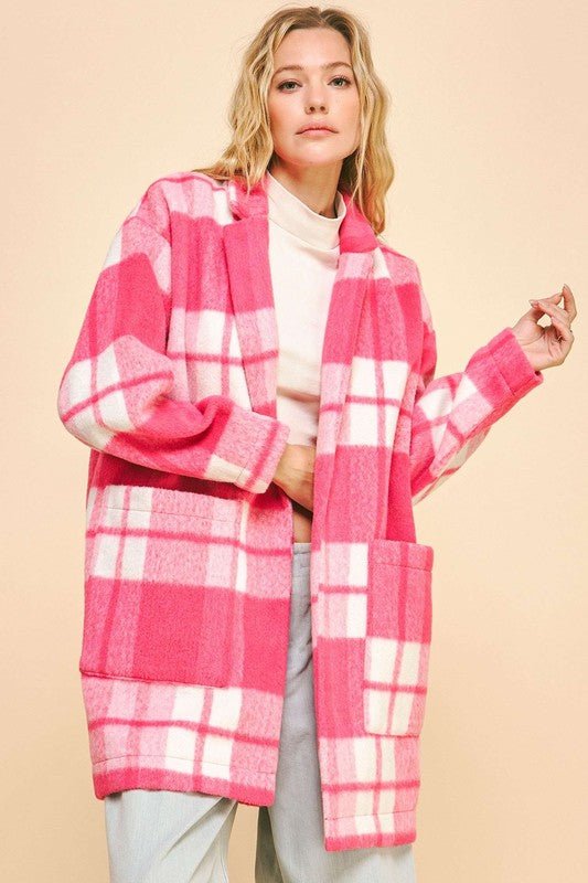 Woman wearing a pink plaid open front longline coat with drop shoulders and pockets.
