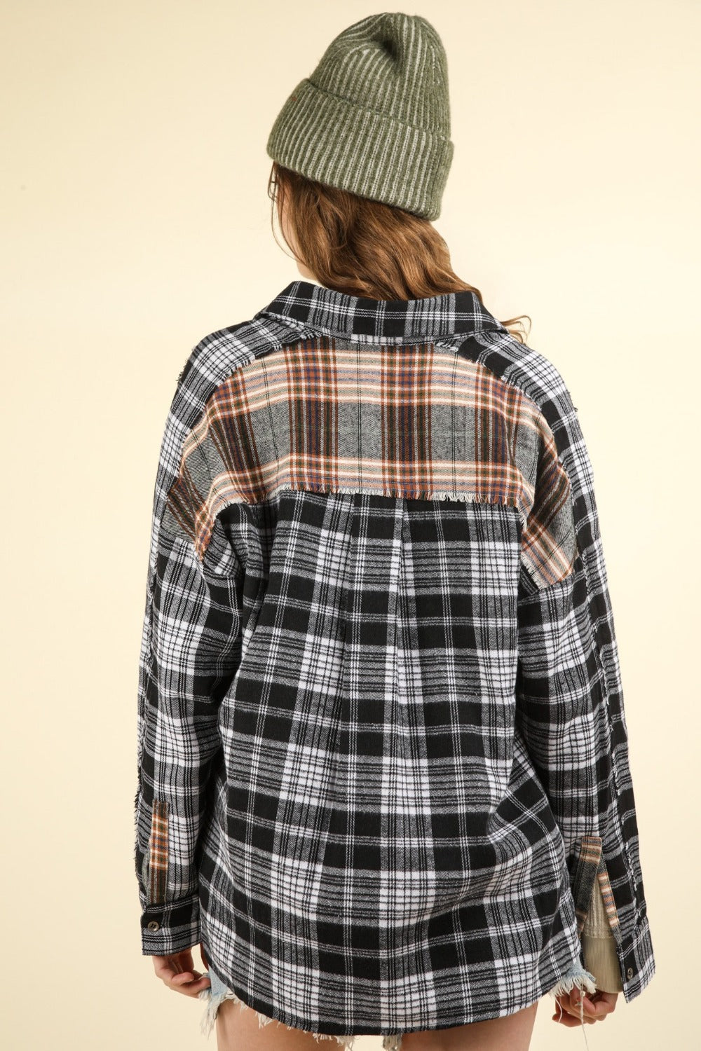 Person wearing oversized black contrast plaid shirt with raw detail, showing back view and green beanie, casual style.