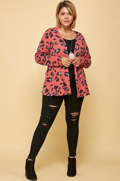 Plus size woman wearing red animal print open front cropped cardigan and black ripped jeans, standing against a beige background.