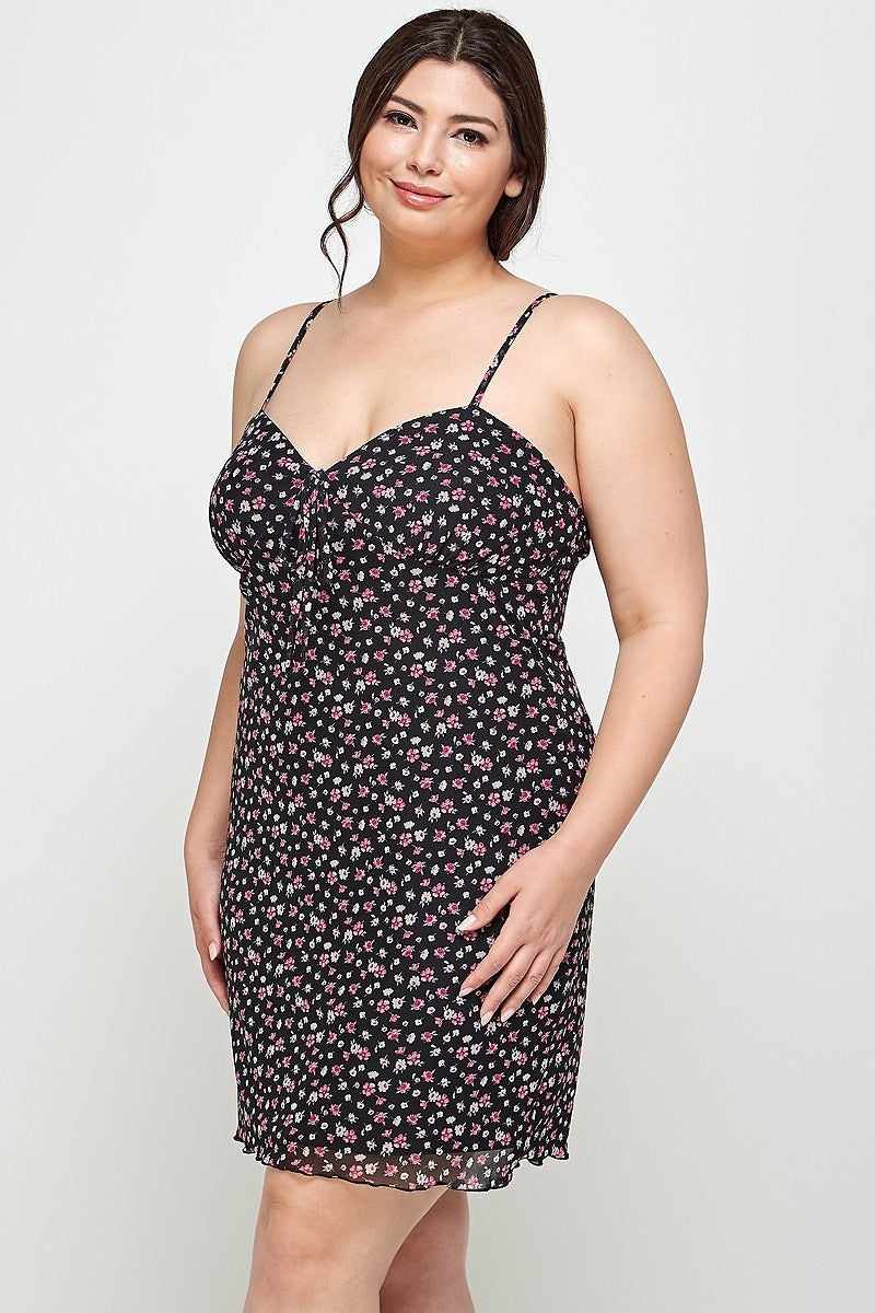 Plus-size woman in a black ditsy floral cami dress with sweetheart neckline and ruffled hem, showcasing confidence and style.