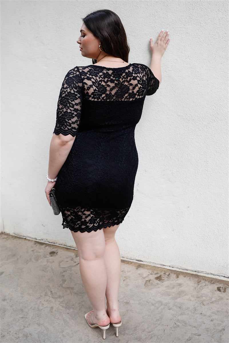 Plus size woman in black lace mini dress with midi sleeves, showcasing elegant and fitted design, standing against a white wall.