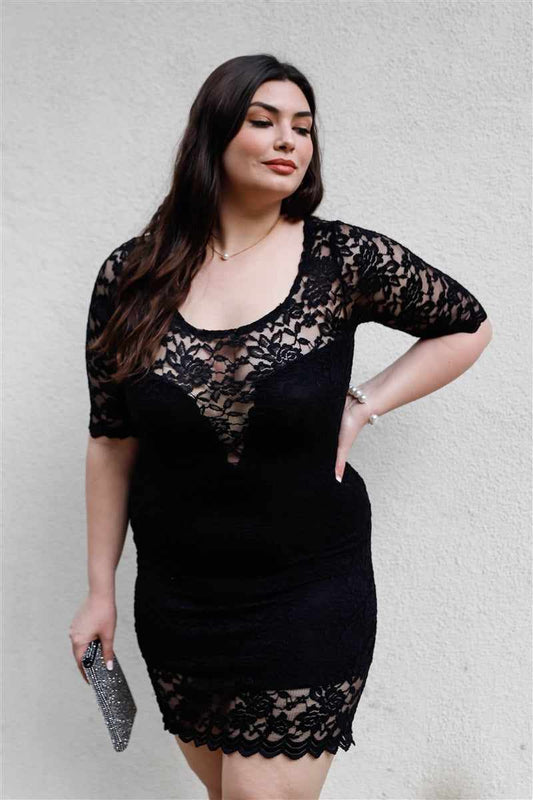 Plus size woman in black lace mini dress with midi sleeves and round neckline, posing confidently against a white background.