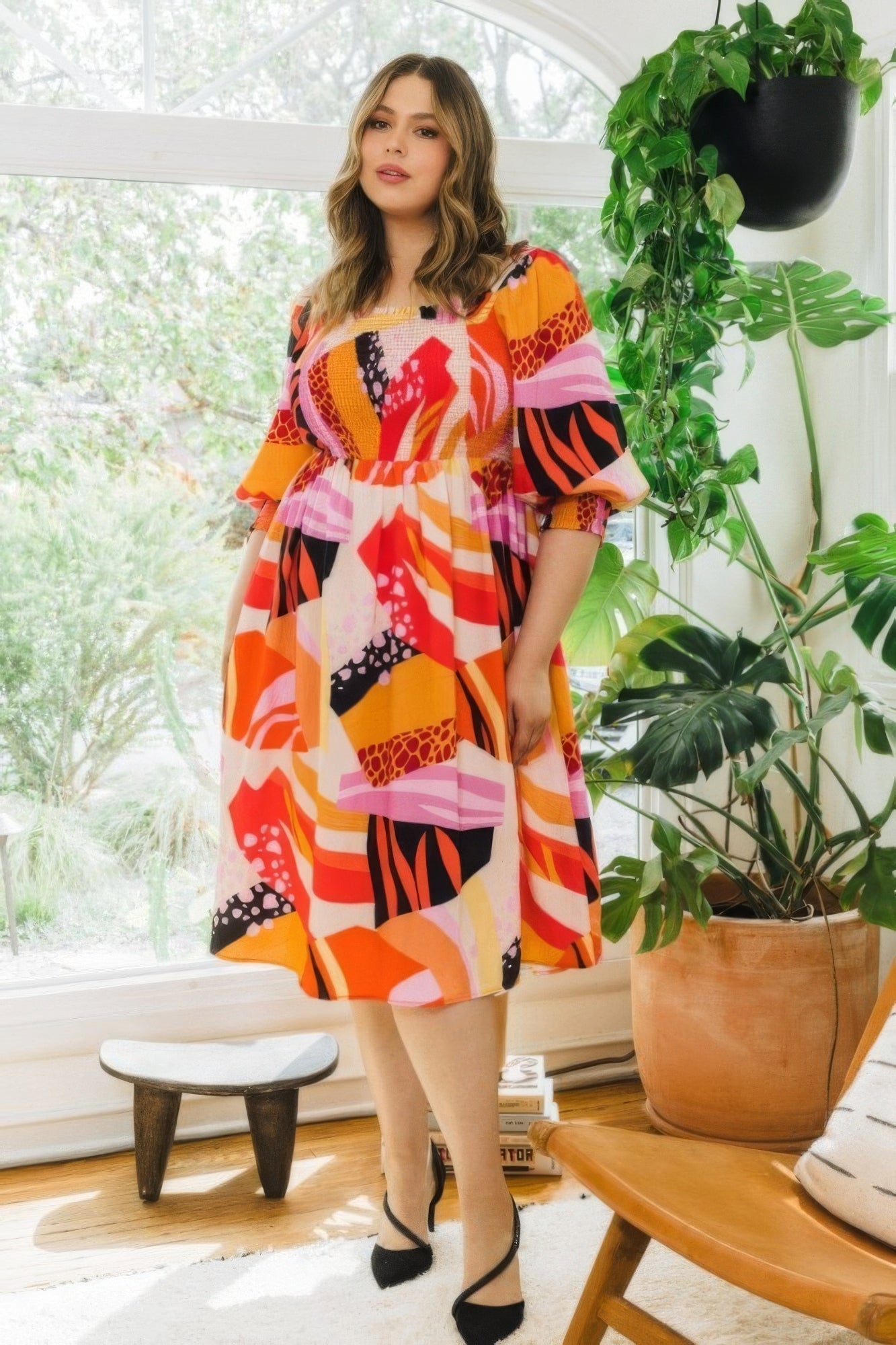 Plus size coral multi floral print square neckline midi dress with 3/4 puff sleeves, worn by a woman standing in a stylish room.