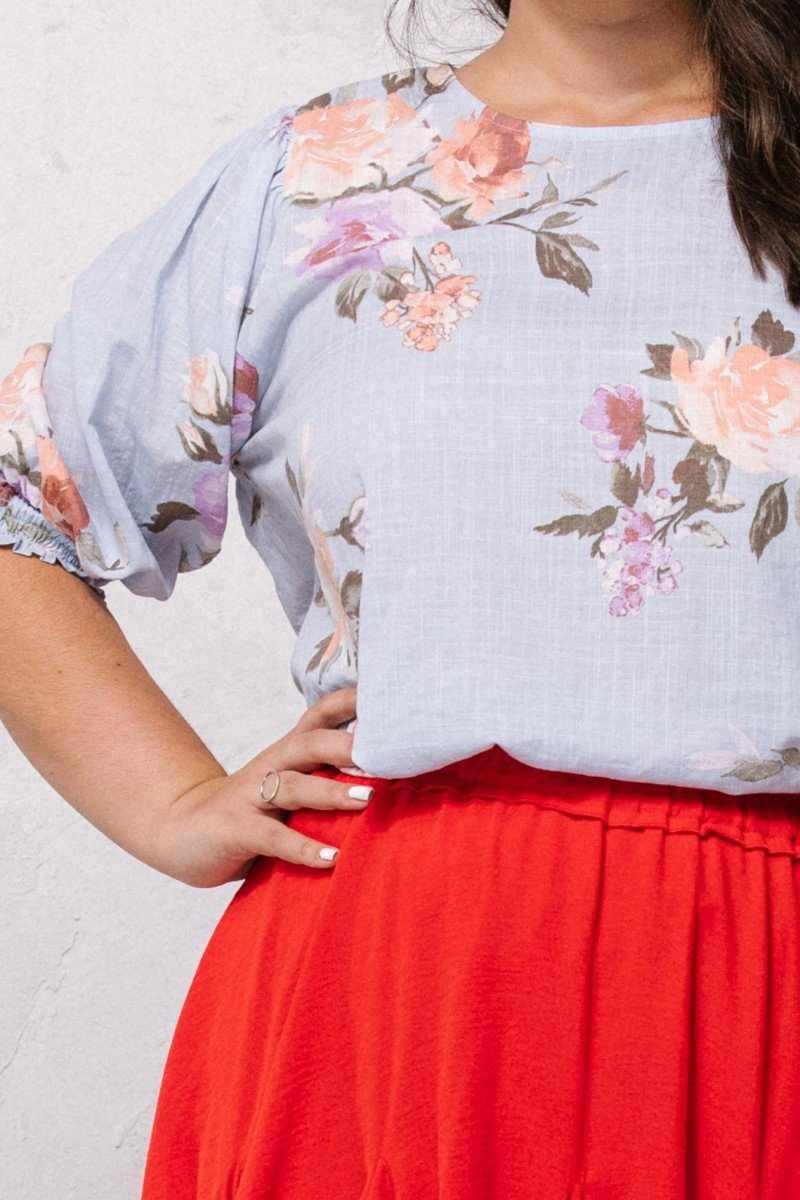 Plus size woman wearing blue floral printed woven blouse with puff sleeves and red skirt.