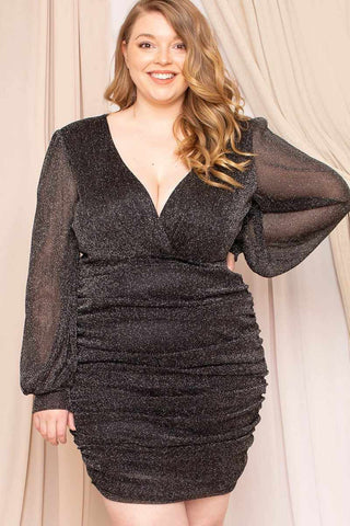 Plus size black glitter mesh mini dress with surplice V-neck and sheer long sleeves, worn by model.