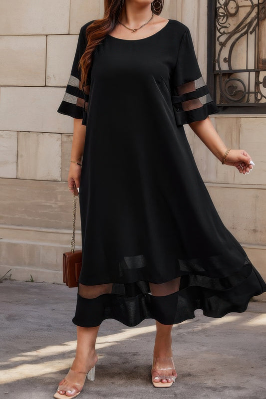 Woman in black midi dress with sheer mesh panel details on sleeves and hem, wearing nude heels and holding brown purse, standing on marble steps.