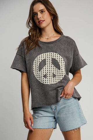 Woman wearing gray vintage-style oversized t-shirt with white checkered peace sign graphic, light blue denim shorts, and layered necklaces against ...