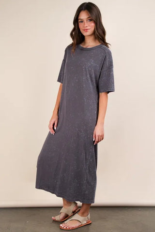 Woman in charcoal gray oversized midi dress with short sleeves and speckled pattern, wearing brown sandals, standing against beige background in re...