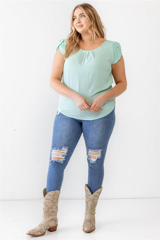 Plus size model wearing mint textured short sleeve blouse with cap sleeves and crew neckline, styled with ripped jeans and cowboy boots.